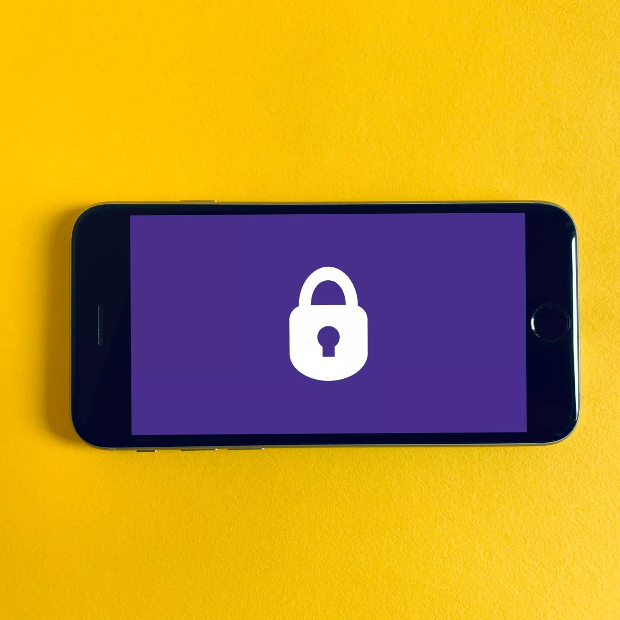 An iPhone, which is photographed against a yellow background, displays a white padlock on a purple screen.