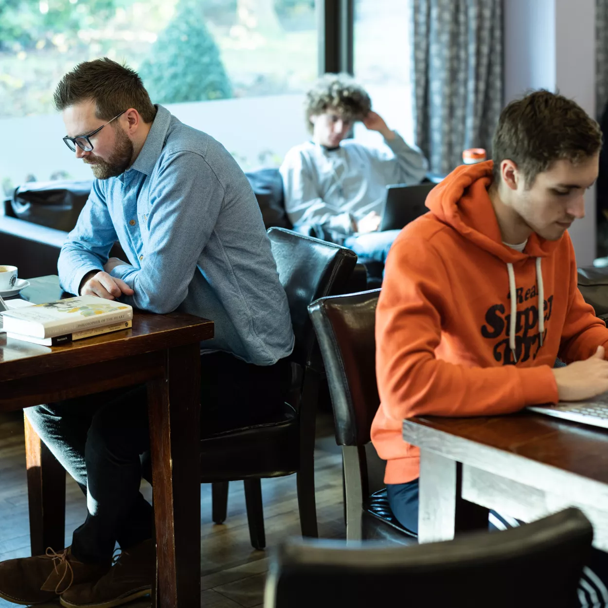 Staff and students are studying at their laptops, seated at different tables in the college cafe