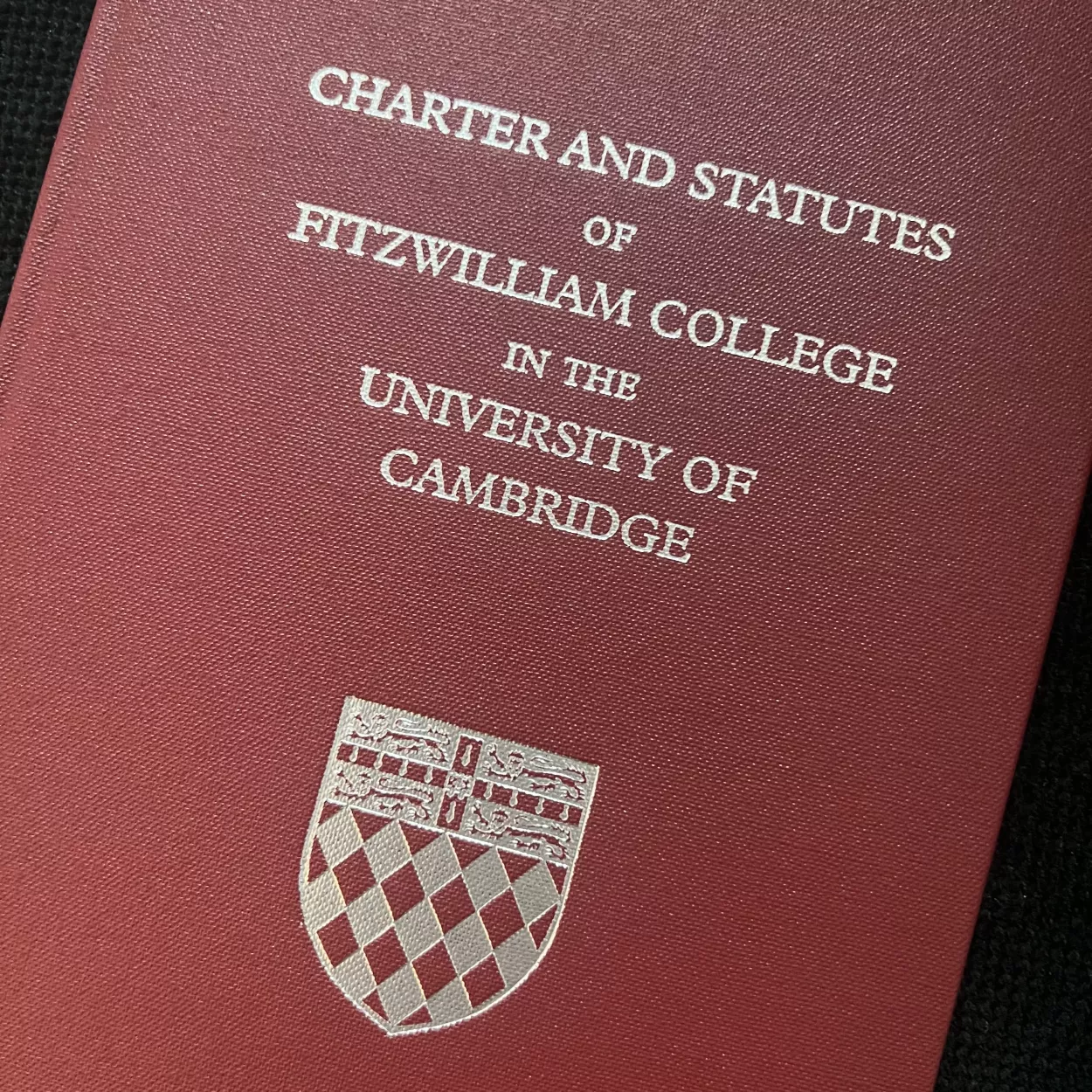 A dark maroon book with the title Charter and Statutes of Fitzwilliam College, in the University of Cambridge, in silver, with the college crest below