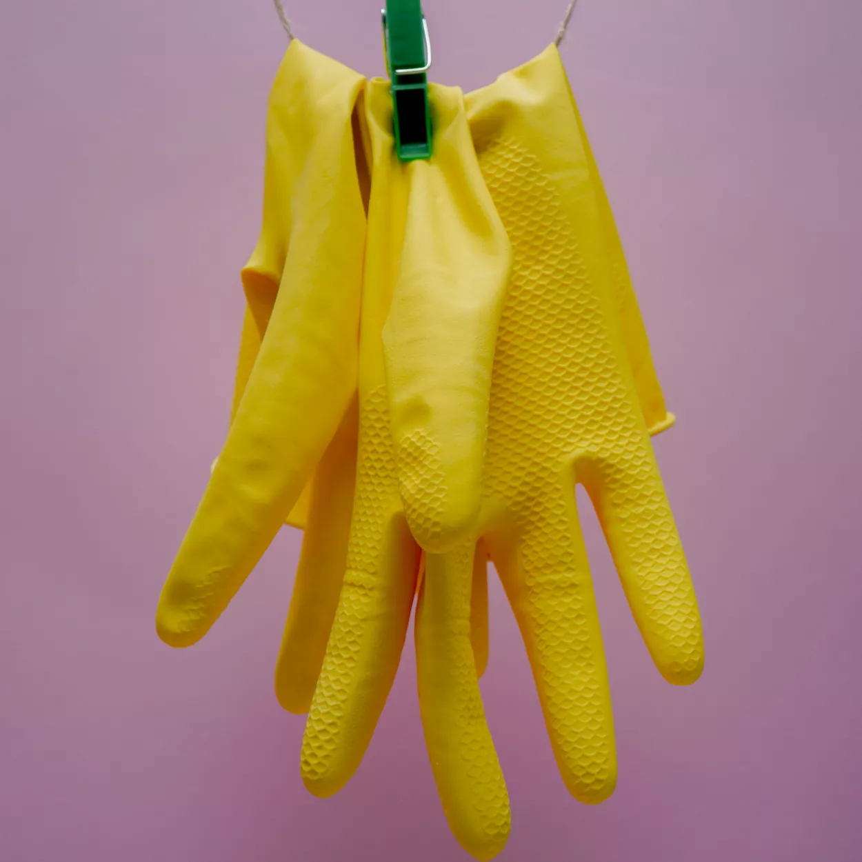 Pair of yellow washing up gloves pegged on a line, on a pink background