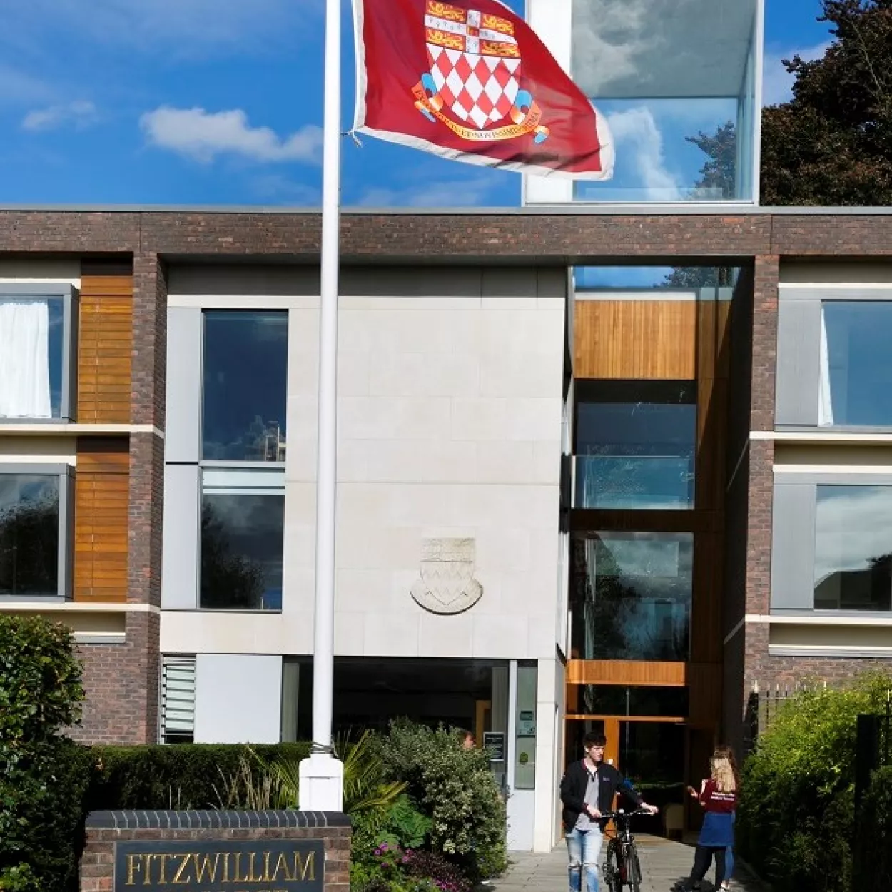 Photo of Fitzwilliam College Porters' Lodge with flag flying of College crest and students entering building